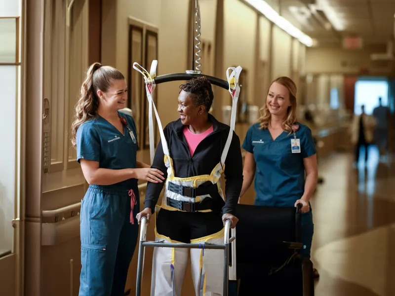 A woman walking with the help of two healthcare workers.