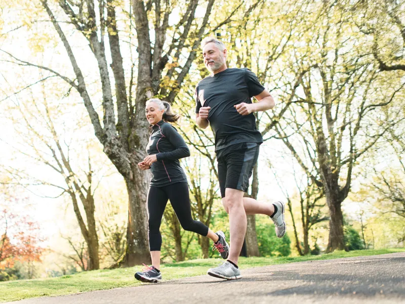 A Middle Aged Couple Jogs Through a Park