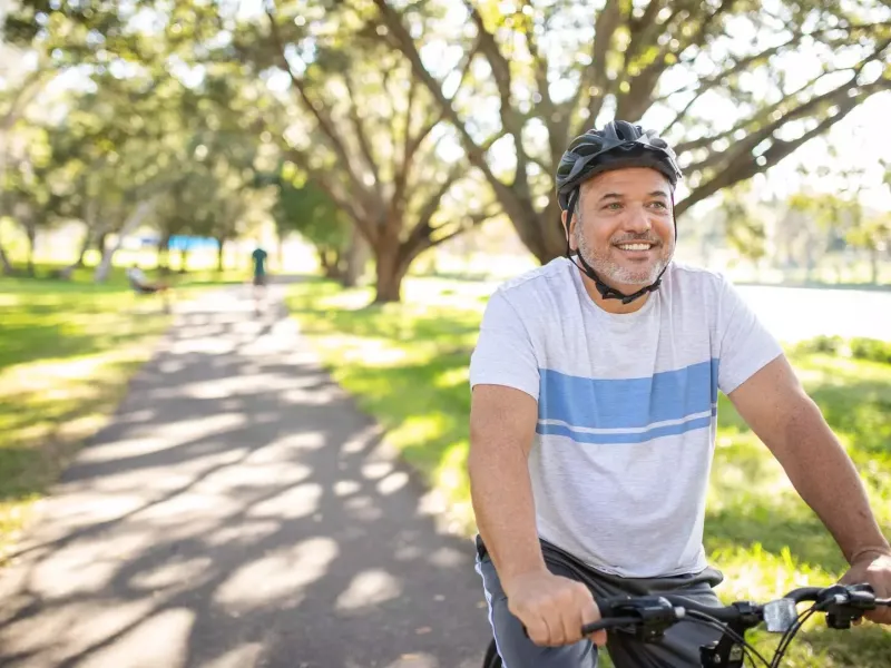 Smiling man riding his bike through the park.