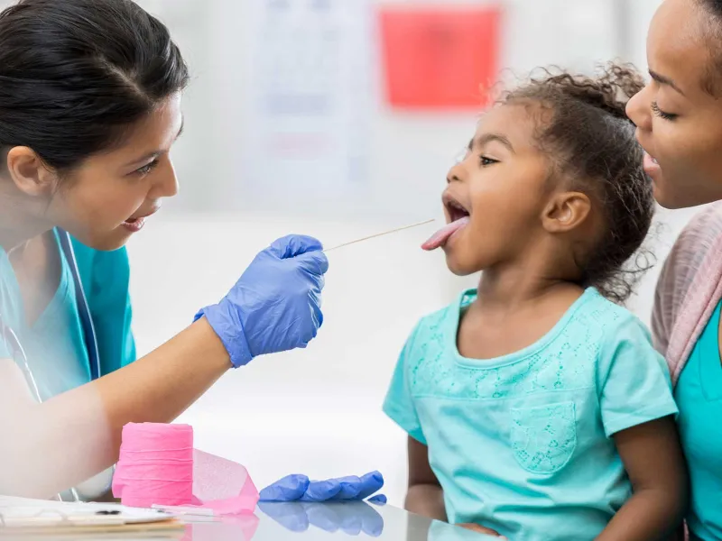 A female nurse examines the tonsils of a young girl at a doctor appointment.