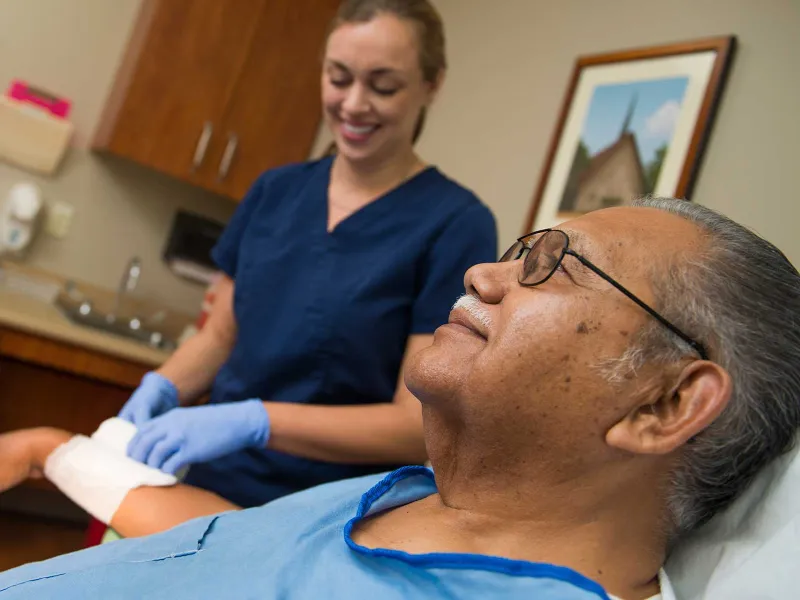 A nurse tends to a Hispanic man's wrist wound.