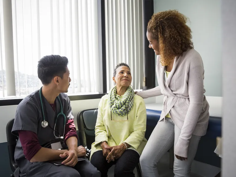 An African American daughter consoles her mother upon hearing medical news from the nurse.