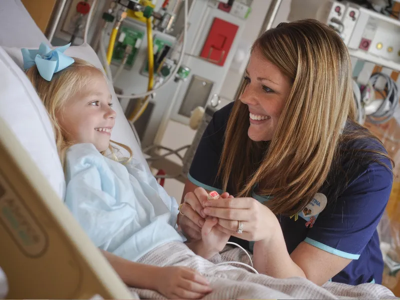 A female nurse consoles a young female patient in her hospital bed.