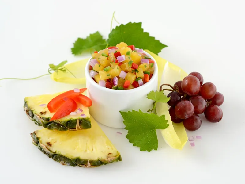 Dish of pineapple and jalapeno salsa surrounded by grapes and greens