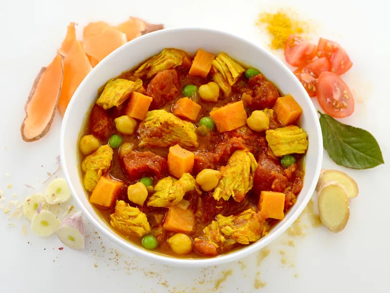 Dish of sweet potato and chicken curry surrounded by chopped potatoes and veggies