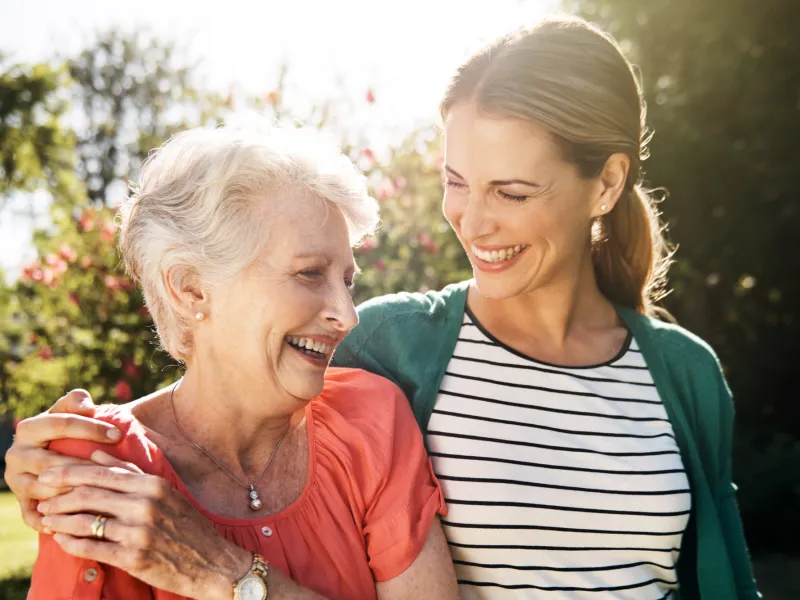 A senior woman with her adult daughter walking together outdoors.