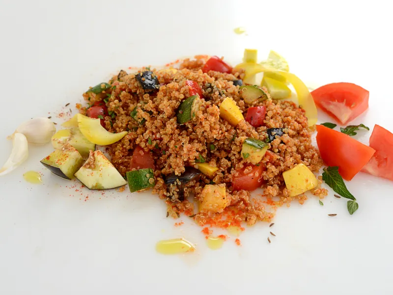 Mound of vegetables and quinoa on white surface with tomato garnish.