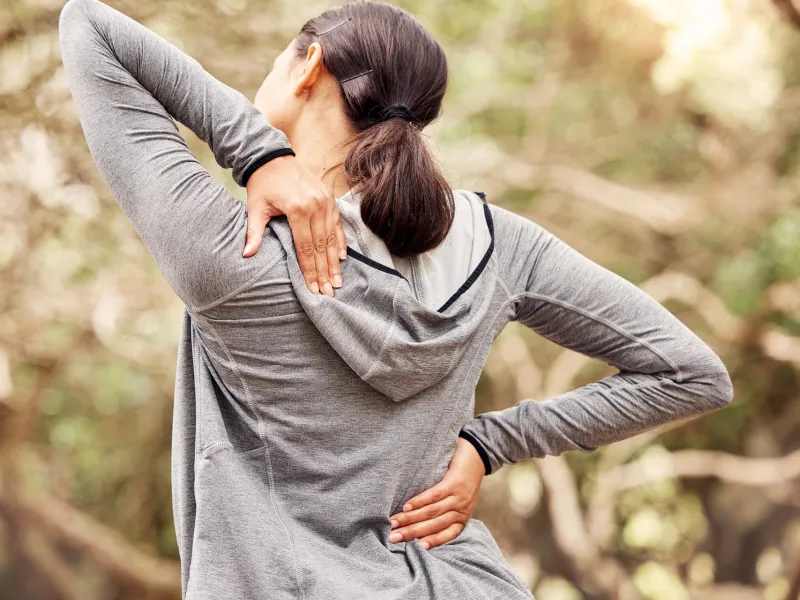 Woman placing hands on back while outside.