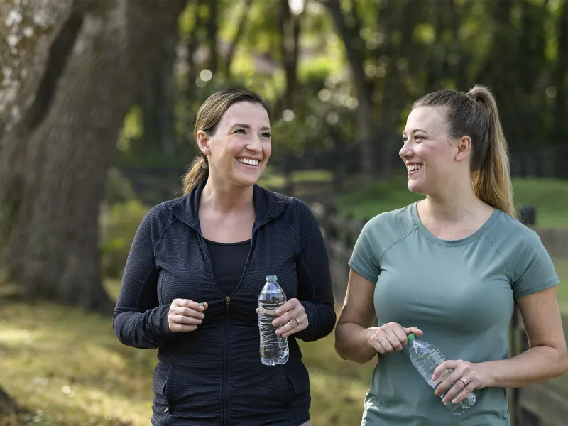 Two women holding water bottles walking together outside 