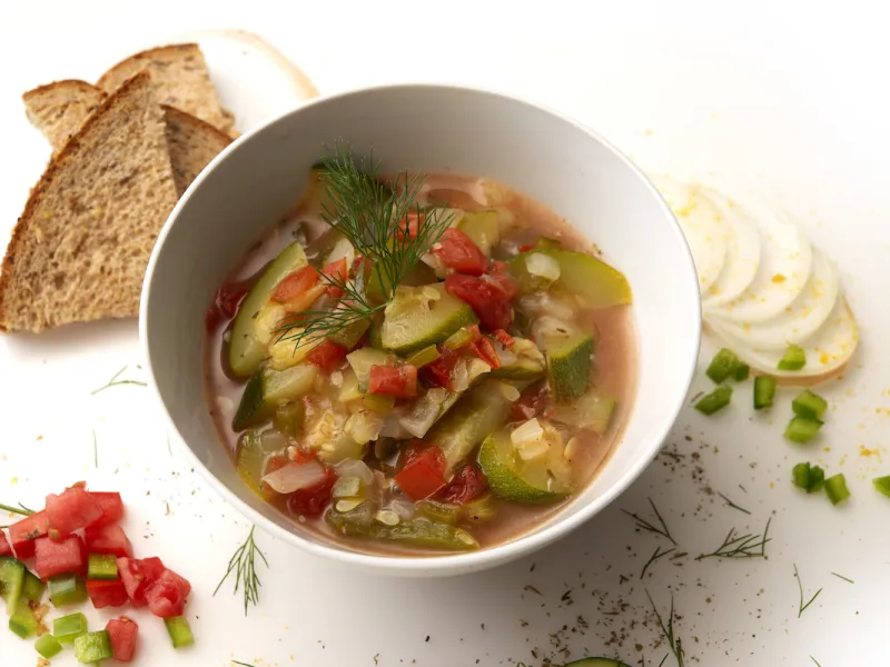 Bowl of zucchini creole with toast and onion, pepper, and herb garnishes