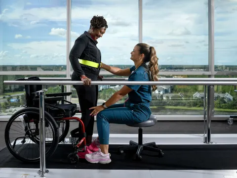 A woman standing up out of a wheelchair with the help of a healthcare worker.