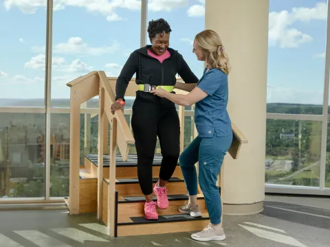 A healthcare worker helping a woman walk down stairs.