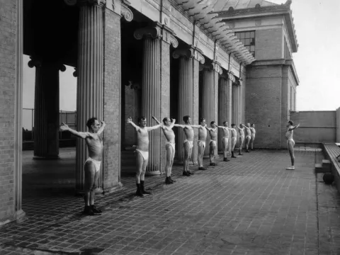 A black and white image of male patients standing outdoors in the sun.