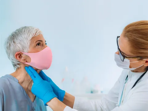 A Doctor examines a patient's neck while they both wear face coverings