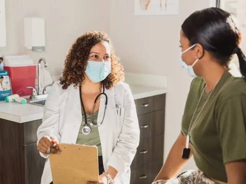 A Doctor Speaks to a Female Military Patient in an Exam Room.