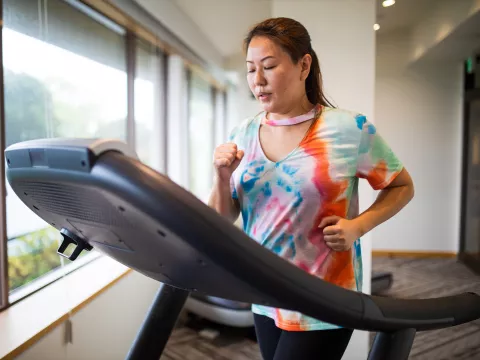 A Woman Jogs on a Treadmill in Front of a Window Overlooking Her Backyard