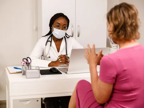 A Doctor Wearing a Face Mask in Her Office Speaks with a Patient about Her Care.