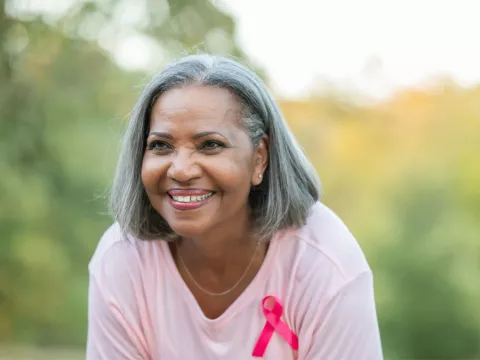 An older woman smiling while wearing a pink shirt and a pink badge