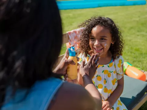 A Mother Applies Sunscreen to Her Smiling Daughter on a Bright Summer Day