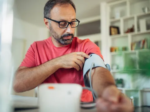 A Man Puts a Blood Pressure Cuff on His Arm in His Home.