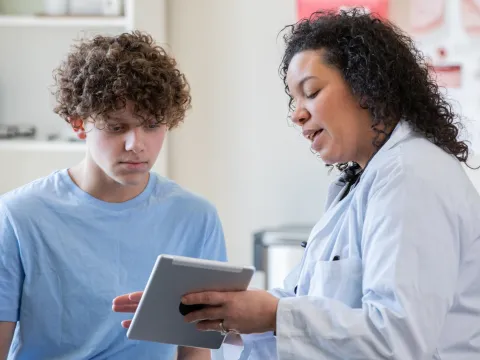 A Physician Goes Over a Teenager's Chart on a Tablet