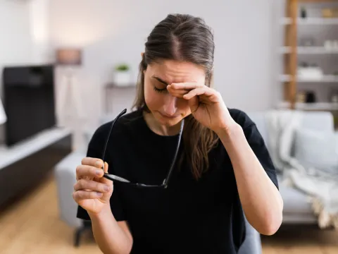 A Woman Rubs the Bridge of Her Nose with Her Eyes Closed.