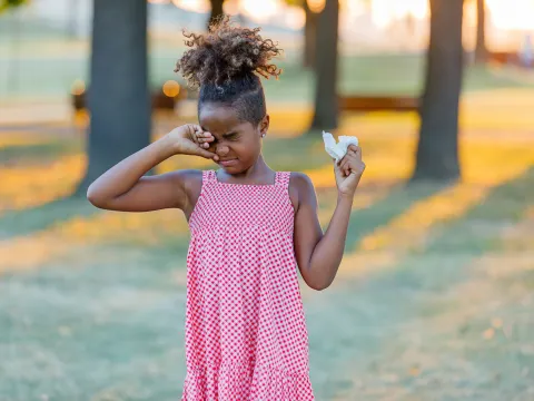 A Child Rubs Her Eye While Walking Through a Park