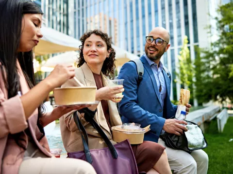 Three Colleagues Sit Outside Enjoying Lunch in the City.