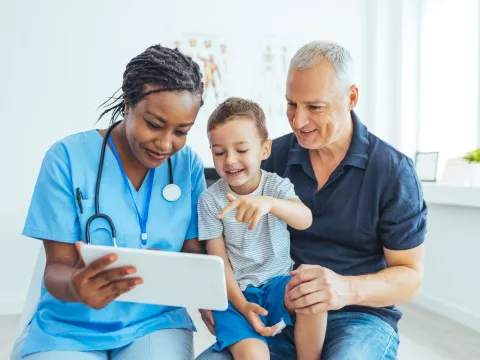 A Doctor Reviews a Patient's Chart with a Pediatric Patient and His Father in an Exam Room.