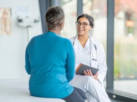 A Smiling Physician Speaks to a Patient in an Exam Room 