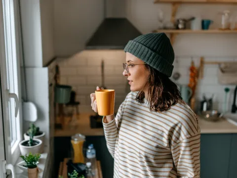 A Woman Enjoys a Hot Beverage While Looking Out the Kitchen Window During the Winter