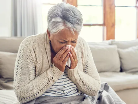 A Senior Woman Blows Her Nose from Seasonal Allergies.