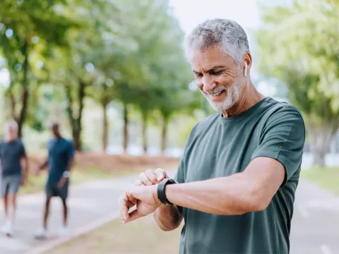A Senior Man Checks His Smart Watch as he Takes a Break from His Walk