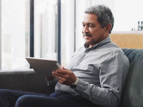 Senior Reading information on a tablet on a sofa