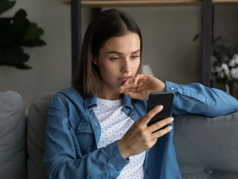 A Young Woman Reads a Message on Her Phone at Home on the Couch
