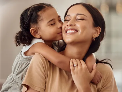 A Daughter Hugs Her Mom While Kissing Her on The Cheek 
