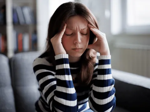 A woman is sitting on a couch with hands resting on the sides of the head.