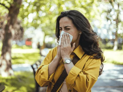 Woman blowing her nose into a tissue outdoors.