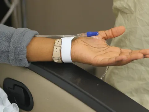 Woman's arm on a chair with infusion needle bandaged onto her wrist 