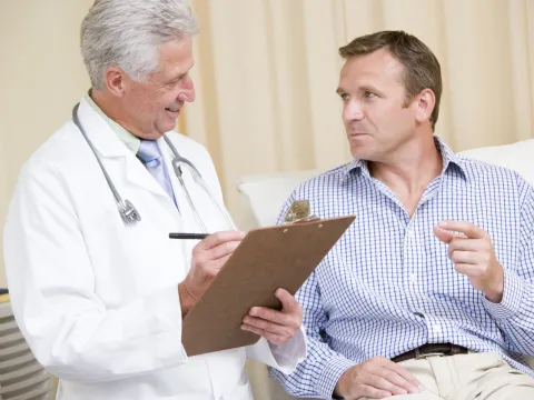 A doctor and his male patient (who is reclined) are consulting during an appointment.