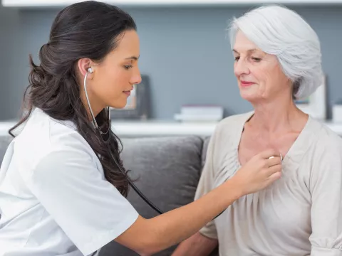 A nurse checks a patient's heart beat as they are both sitting down.