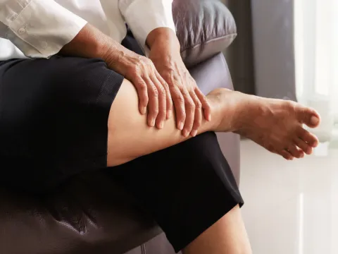 A person sitting down massaging their calf due to pain.