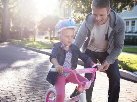 Father teaching his young daughter how to ride a pink bike in the street.
