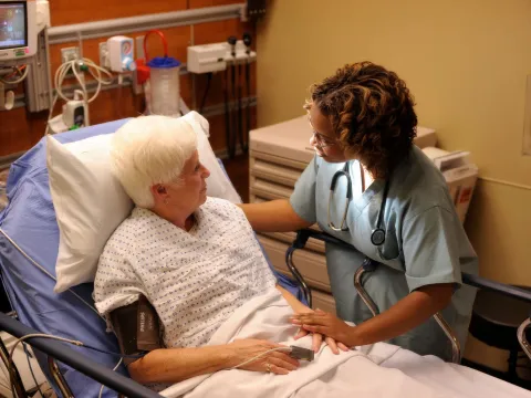 An older woman laying in a hospital bed talking to a nurse.