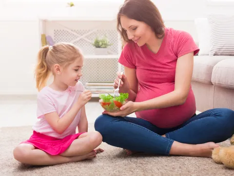 A pregnant mother teaching her daughter healthy eating habits