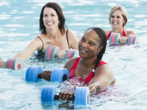 Three women building knee strength in a water aerobics class.