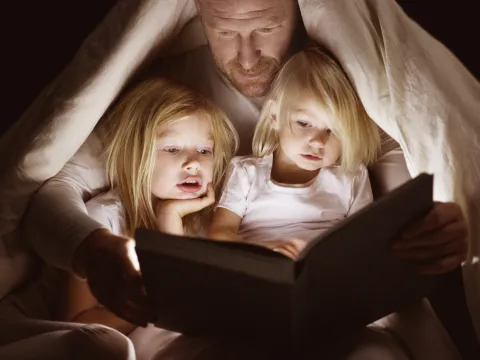 A dad reads to his daughters by flashlight.