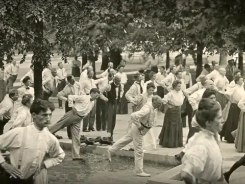 Old photograph of people balancing on one leg and stretching outdoors. 