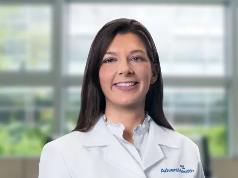 Amanda Robinson, DO, smiles at the camera. She is a white woman with brunette hair and is wearing a white medical coat.
