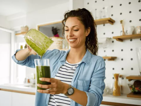 A woman pouring a green smoothie into a cup.
